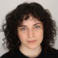 a person with curly hair faintly smiling at the camera