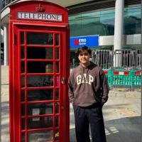 a person in a sweatshirt standing next to a red phone booth
