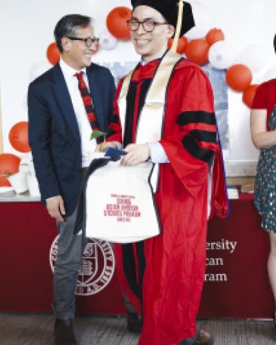a graduating student in a red robe smiles at the camera